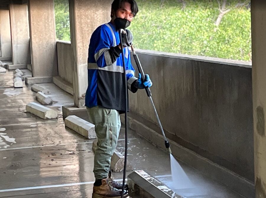 Crew member wand-washing the base of a garage wall at sunrise