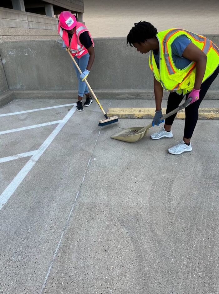 Two crew members sweeping debris from a rooftop garage deck