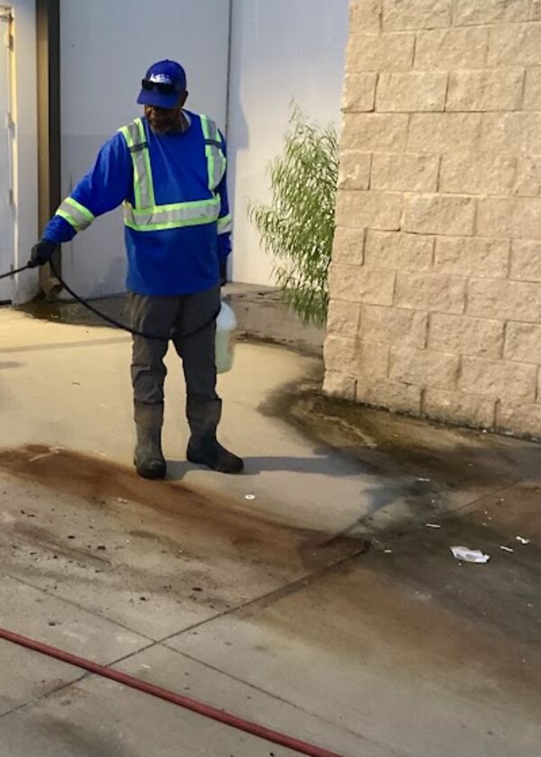 Crew member pre-treating a grease stain on concrete behind a retail store at night
