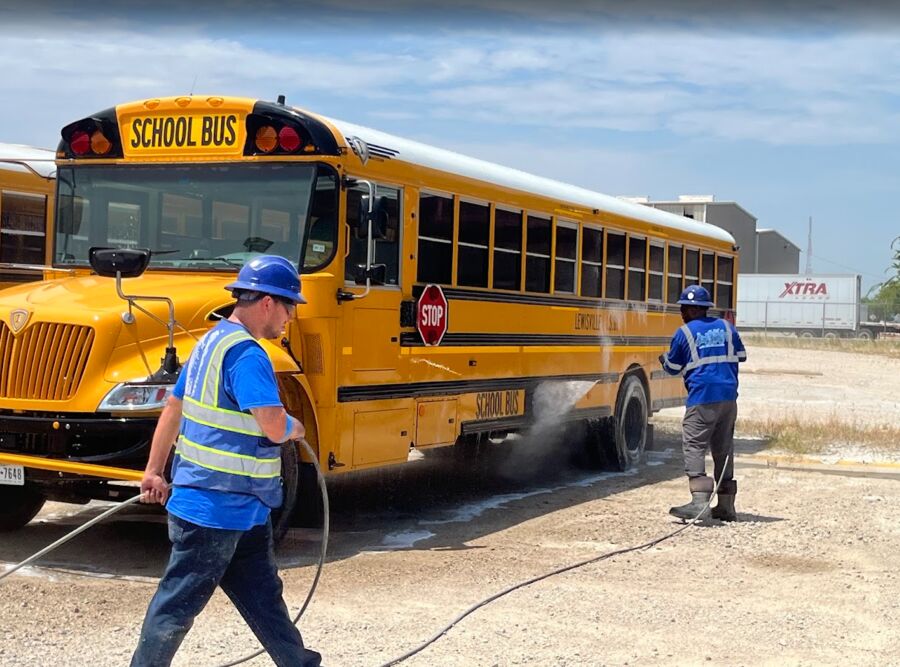 Two crew members pressure washing a yellow school bus