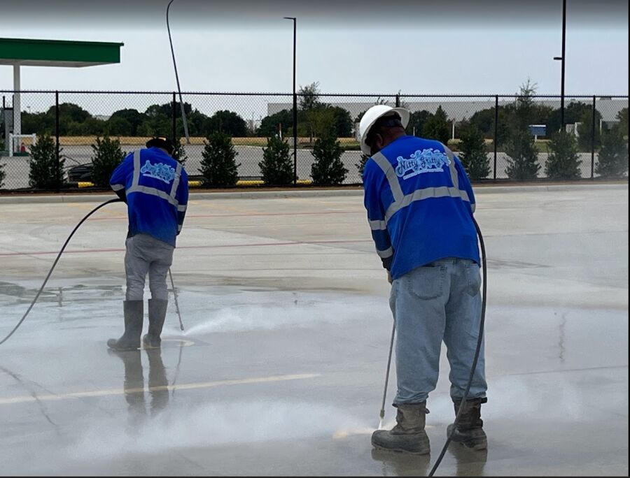 Two crew members pressure washing new concrete at a commercial site
